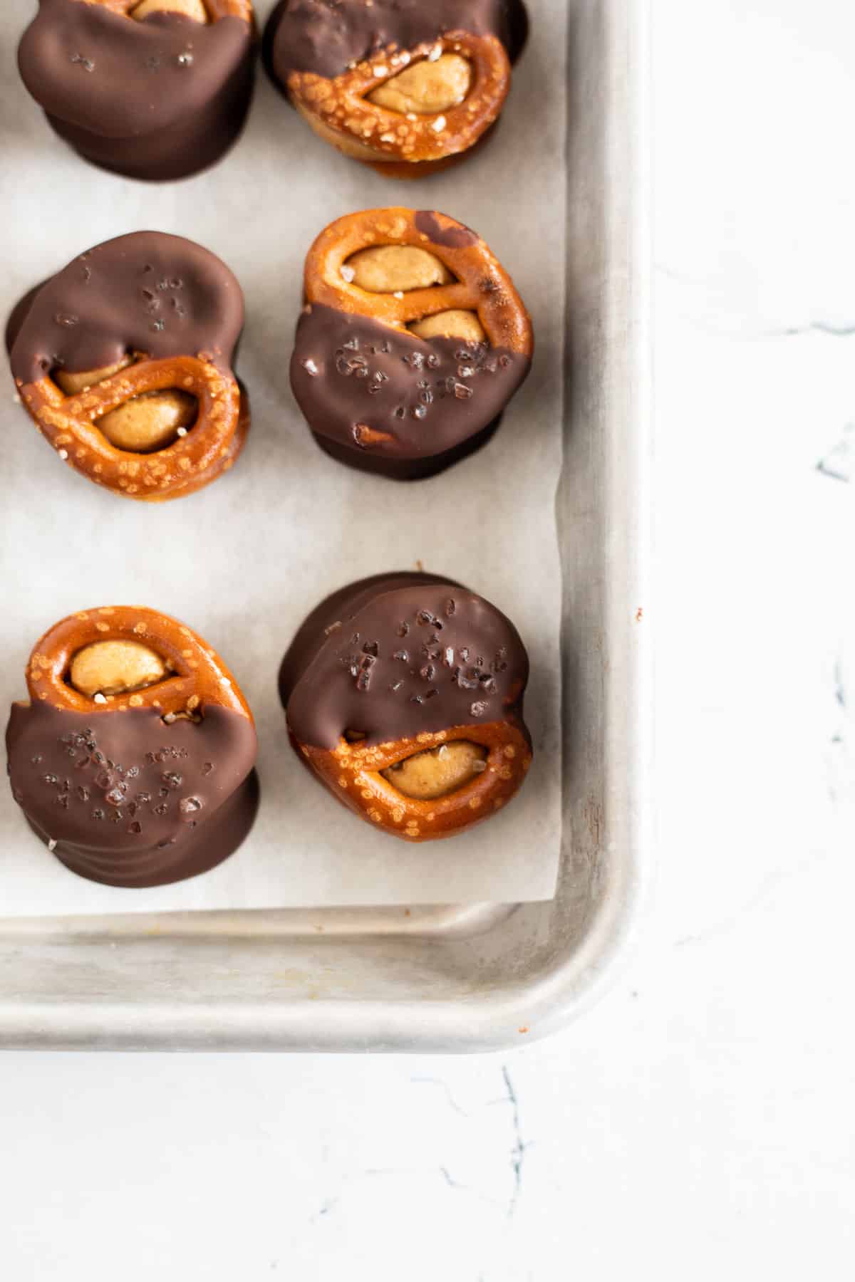 Peanut Butter Pretzel Bites with half dipped in chocolate on a parchment lined baking sheet.