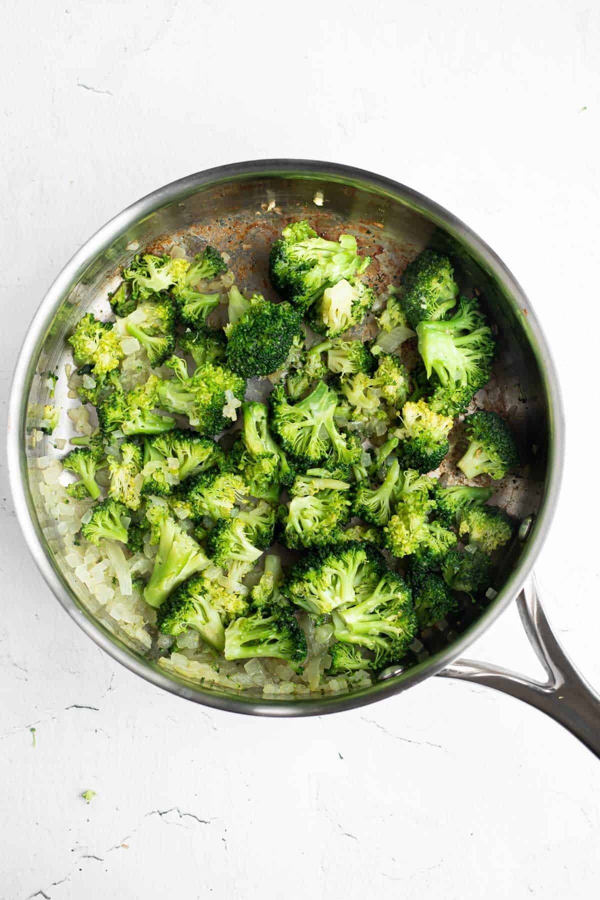 sauteed broccoli and onion in a stainless steel pan.
