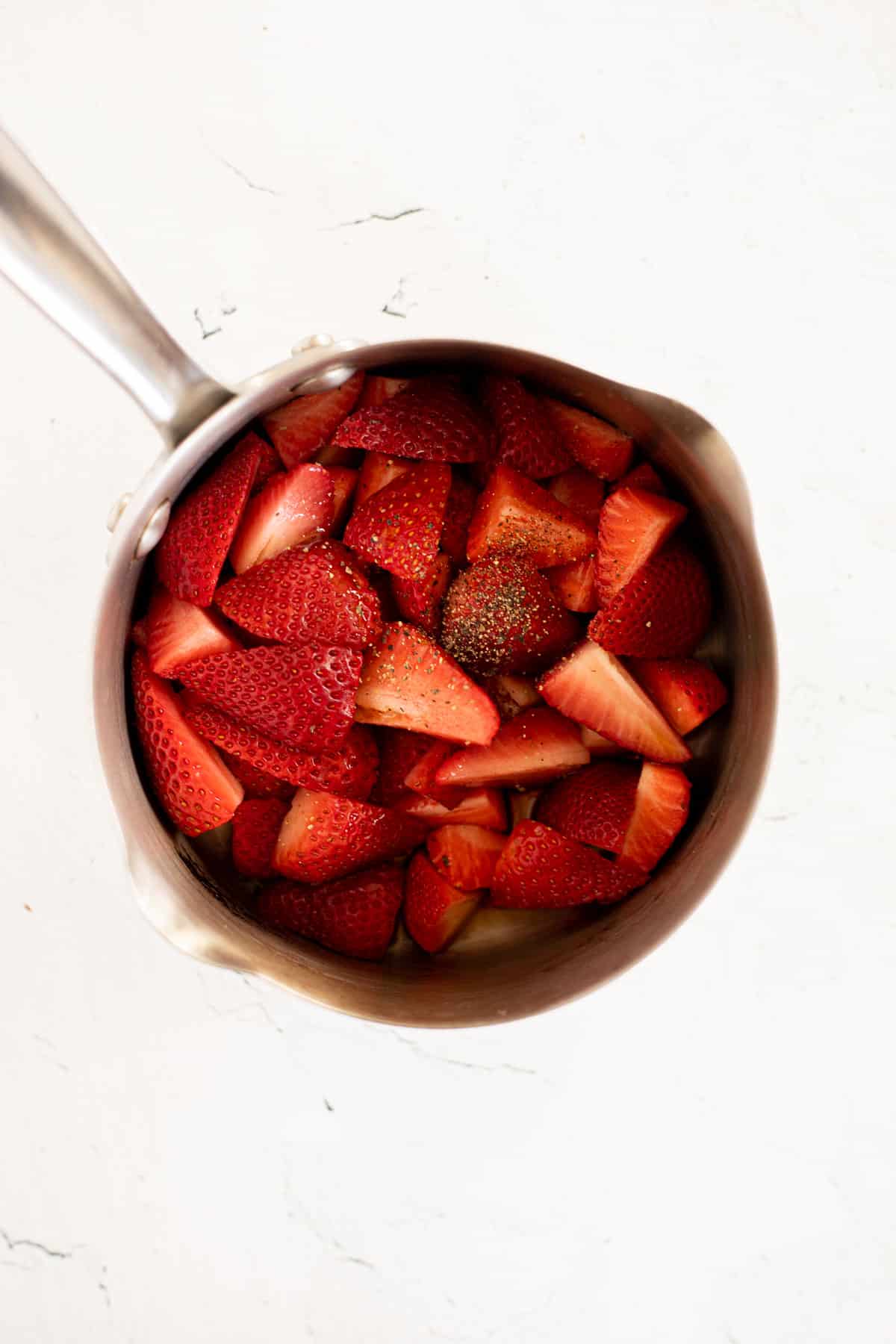 quartered strawberries and maple syrup in a silver pot.