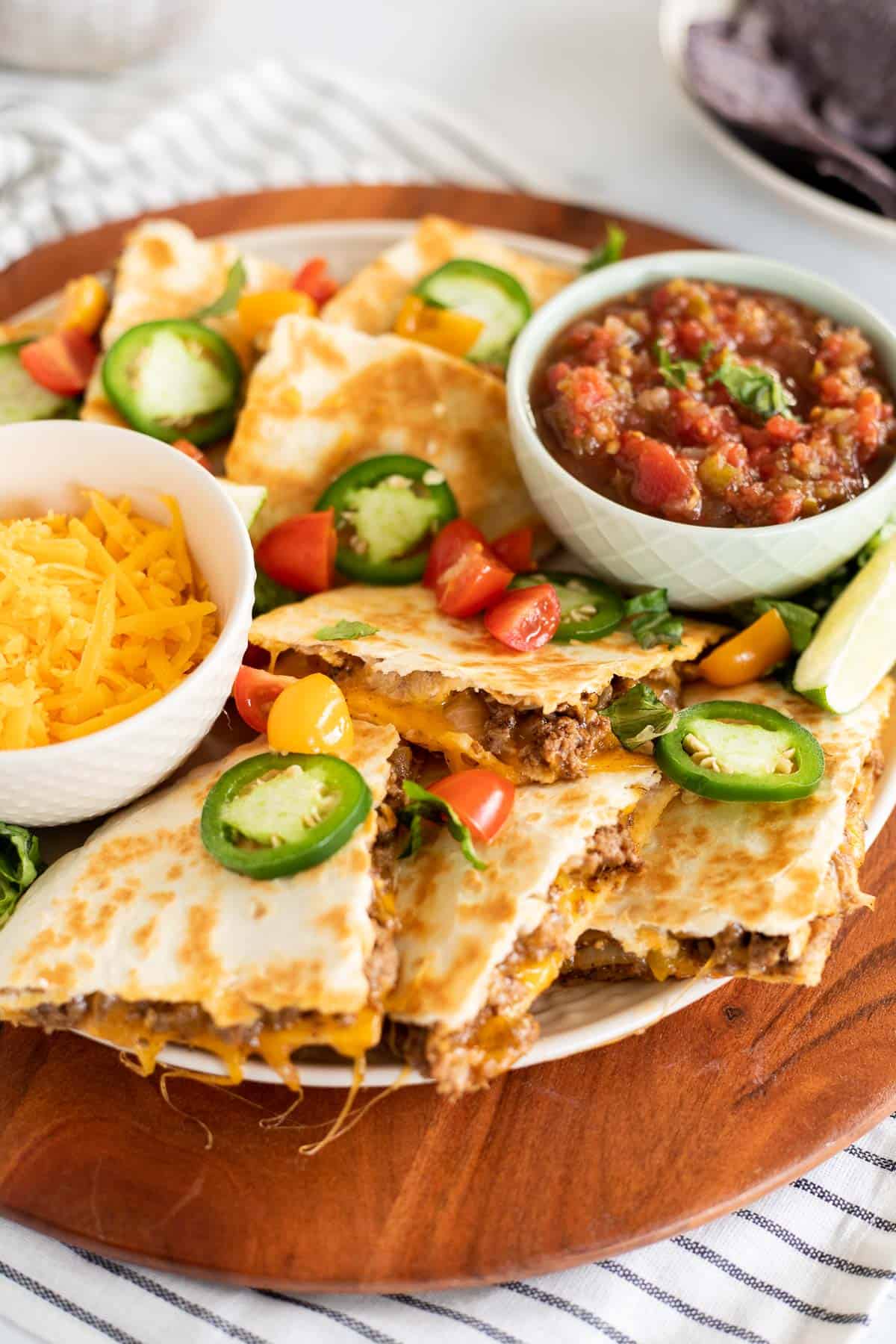 platter of cheesy ground beef quesadillas with sliced jalapenos and tomatoes.