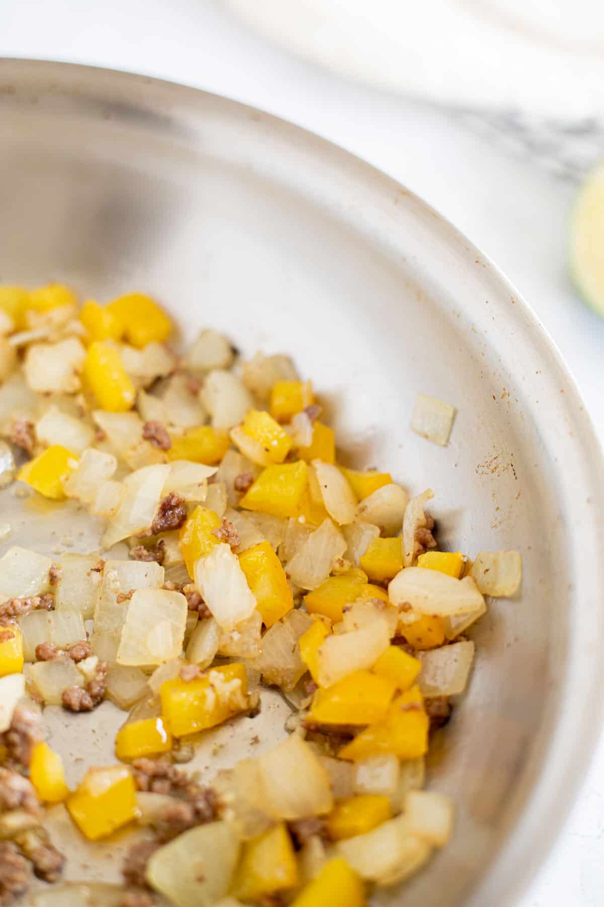 diced onion and yellow pepper cooked in a stainless steel pan.