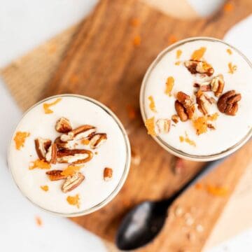 two jars of carrot cake overnight oats topped with yogurt and chopped pecans on a wooden board.