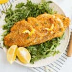 air fryer chicken cutlets on a bed of arugula with a lemon wedge.