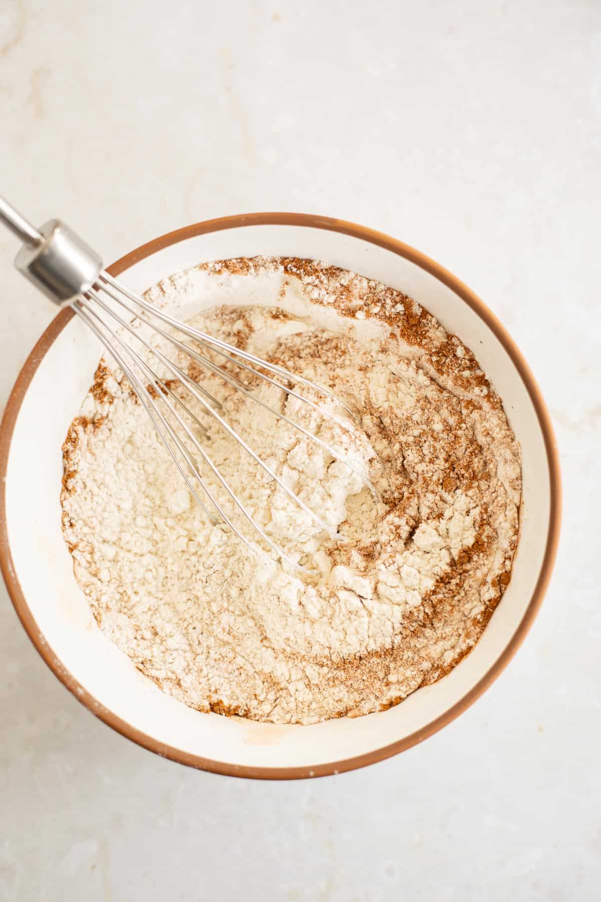 flour, baking soda, and spices in a white bowl with a whisk.