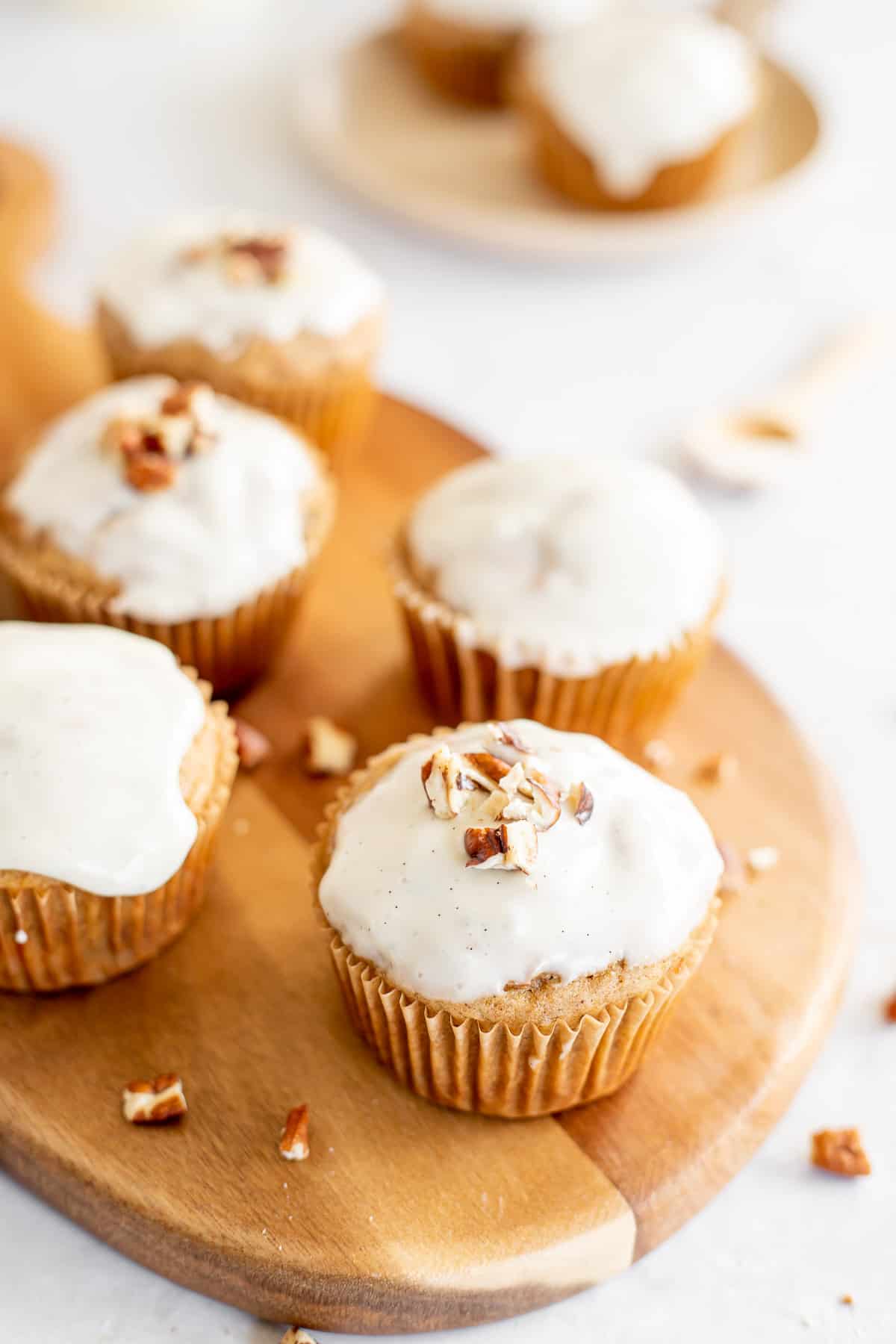 carrot cake muffins with a vanilla glaze on a wooden cutting board.