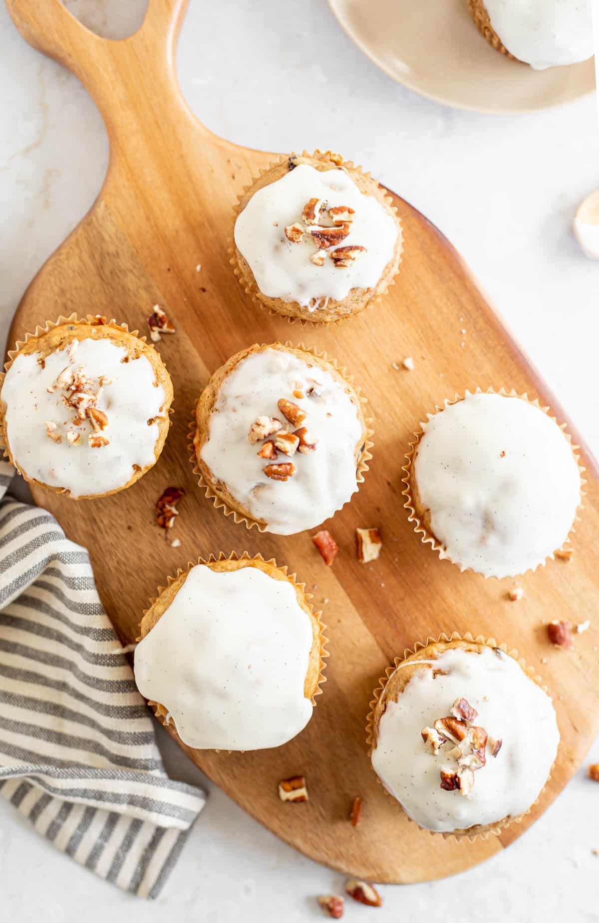 overhead view of carrot cake muffins with a vanilla glaze on a wooden serving board.