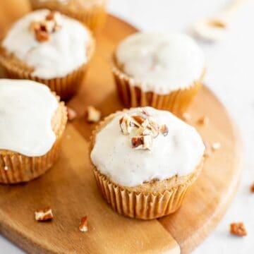 carrot cake muffins with a vanilla glaze on a wooden cutting board.