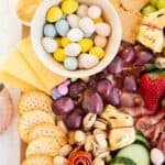 an Easter charcuterie board highlighting fruit, veggies, crackers, deviled eggs, and pastel candies.