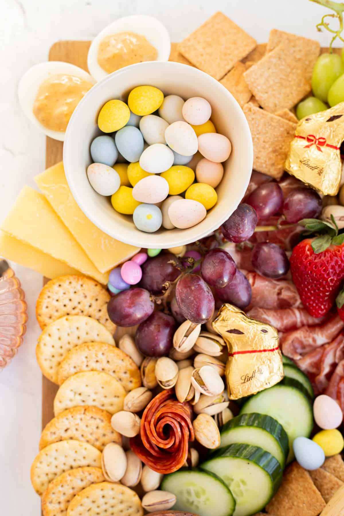 an Easter charcuterie board highlighting fruit, veggies, crackers, deviled eggs, and pastel candies.