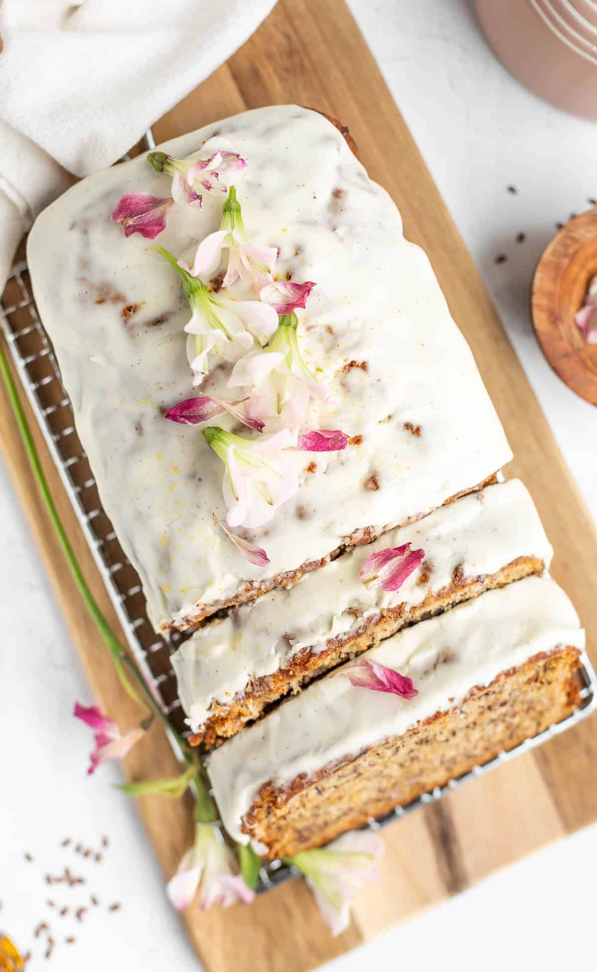 glazed eggless banana bread topped with flower petals on a wooden board.