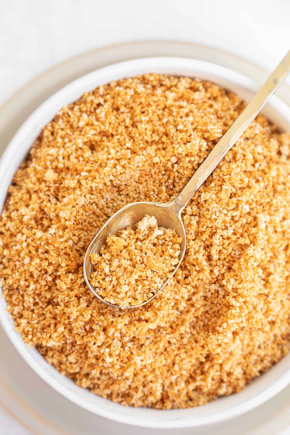 browned gluten free bread crumbs in a white bowl with a spoon.