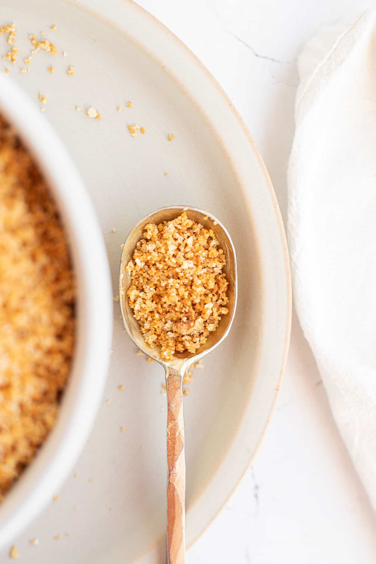 a gold spoon with gluten free bread crumbs on a tan plate.