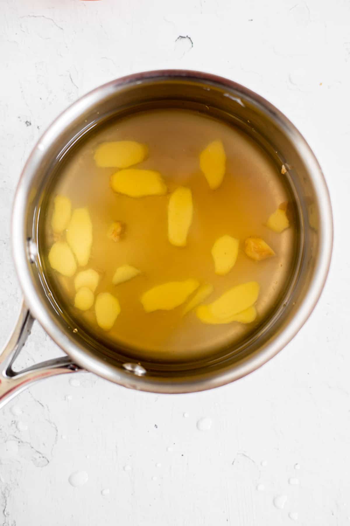 water, honey, and fresh ginger slices in a silver pot.
