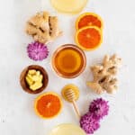 honey ginger tea flat lay picture with fresh ginger, orange slices, honey, and purple flowers.
