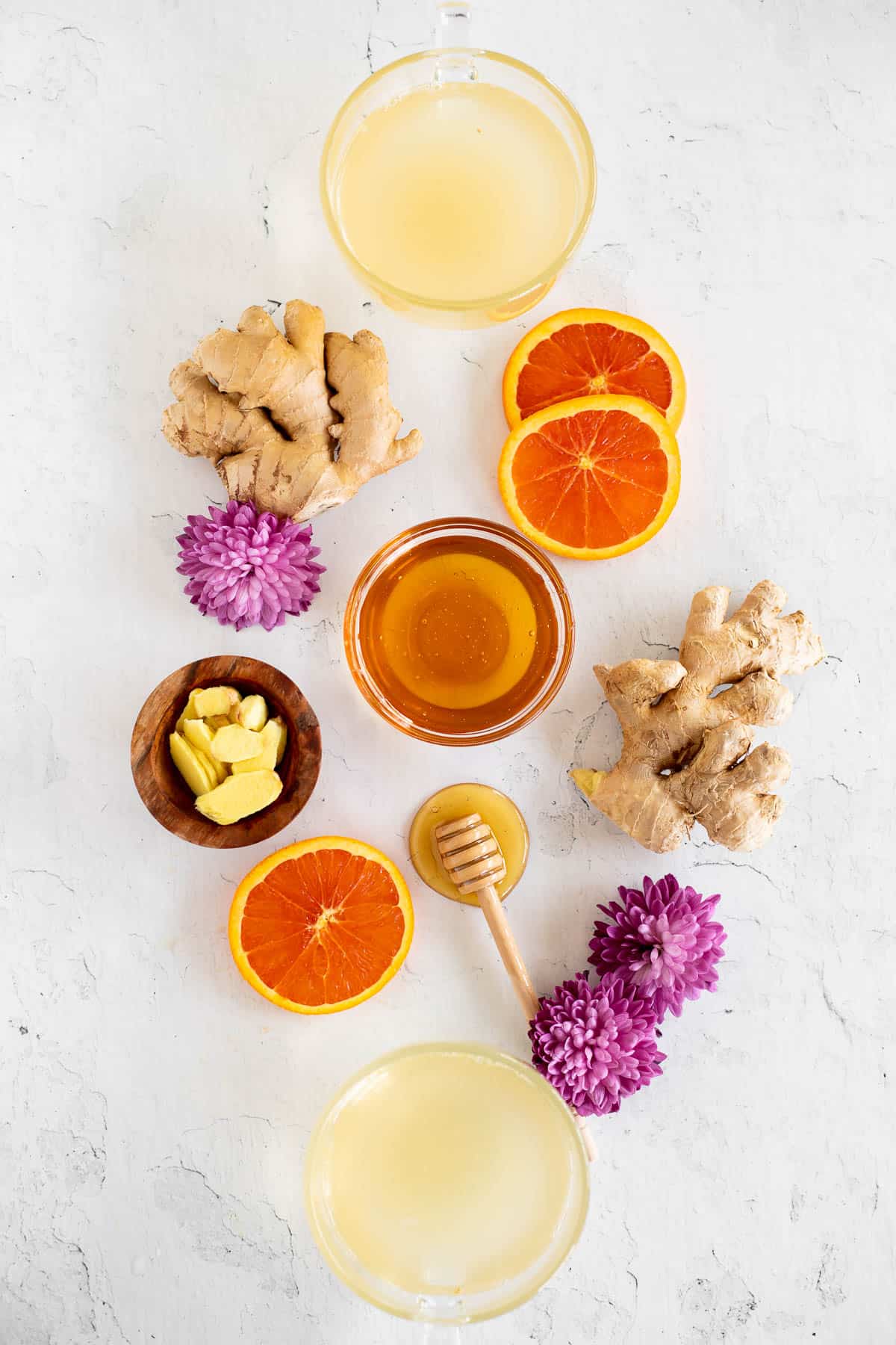 flat lay picture with mugs of tea, fresh ginger, orange slices, honey, and purple flowers.