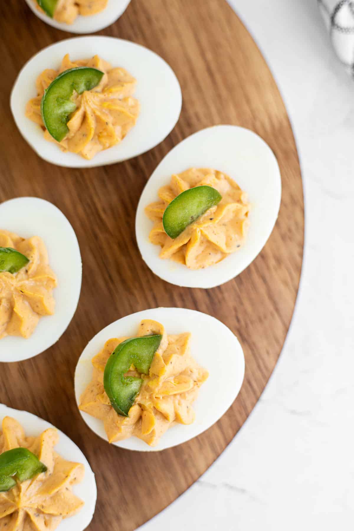 deviled eggs with buffalo sauce garnished with a jalapeno on a wooden platter.