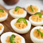 spicy deviled eggs garnished with jalapenos on a wooden serving platter.
