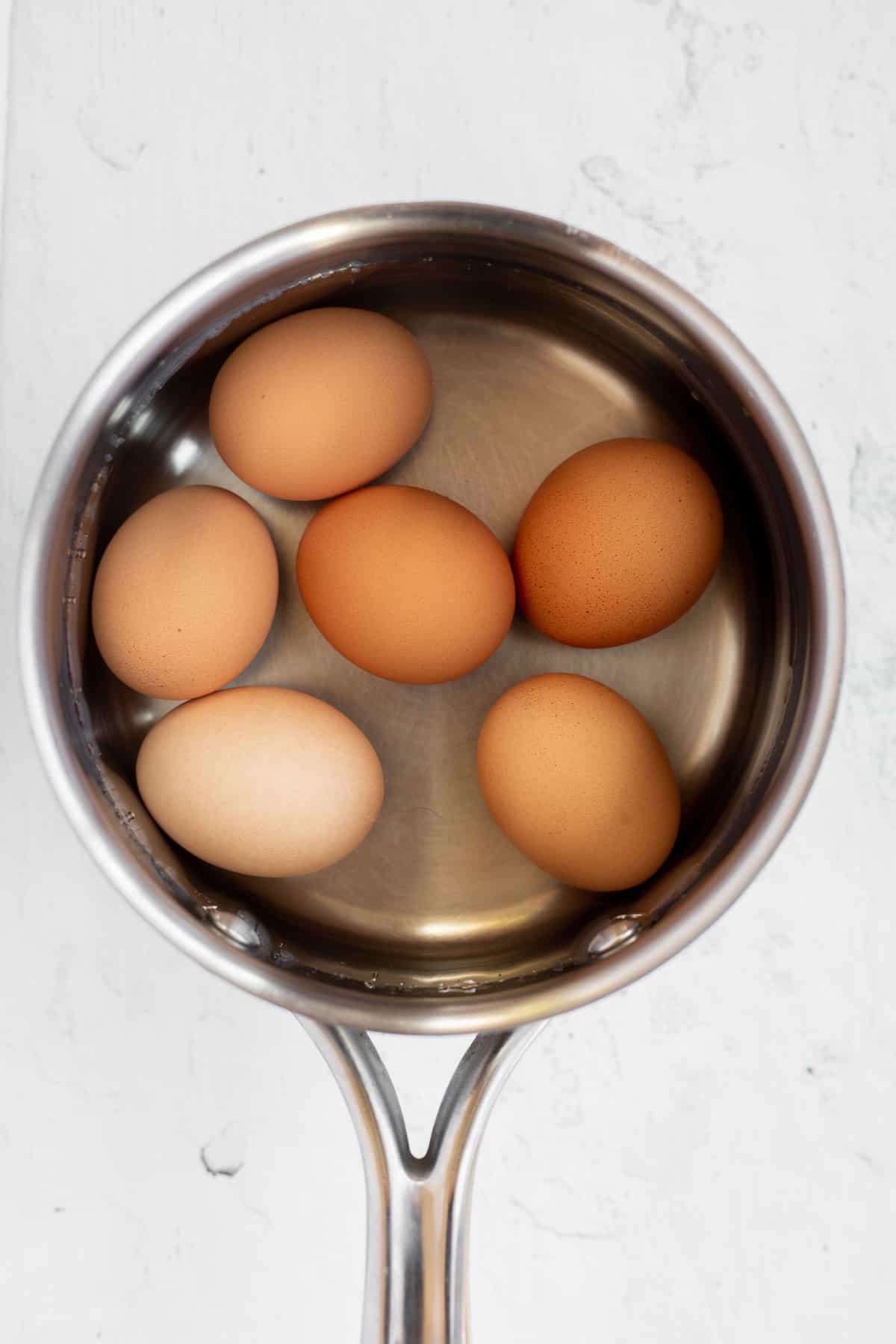 3 brown eggs in a pot of water.