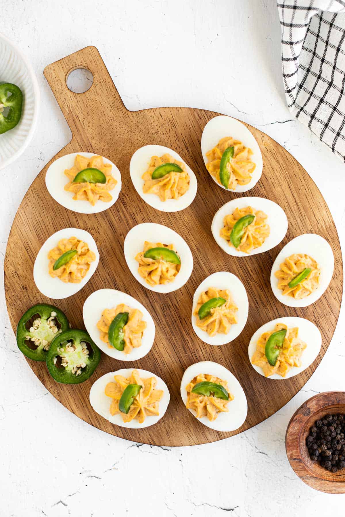 twelve spicy deviled eggs on a round, wooden serving platter.