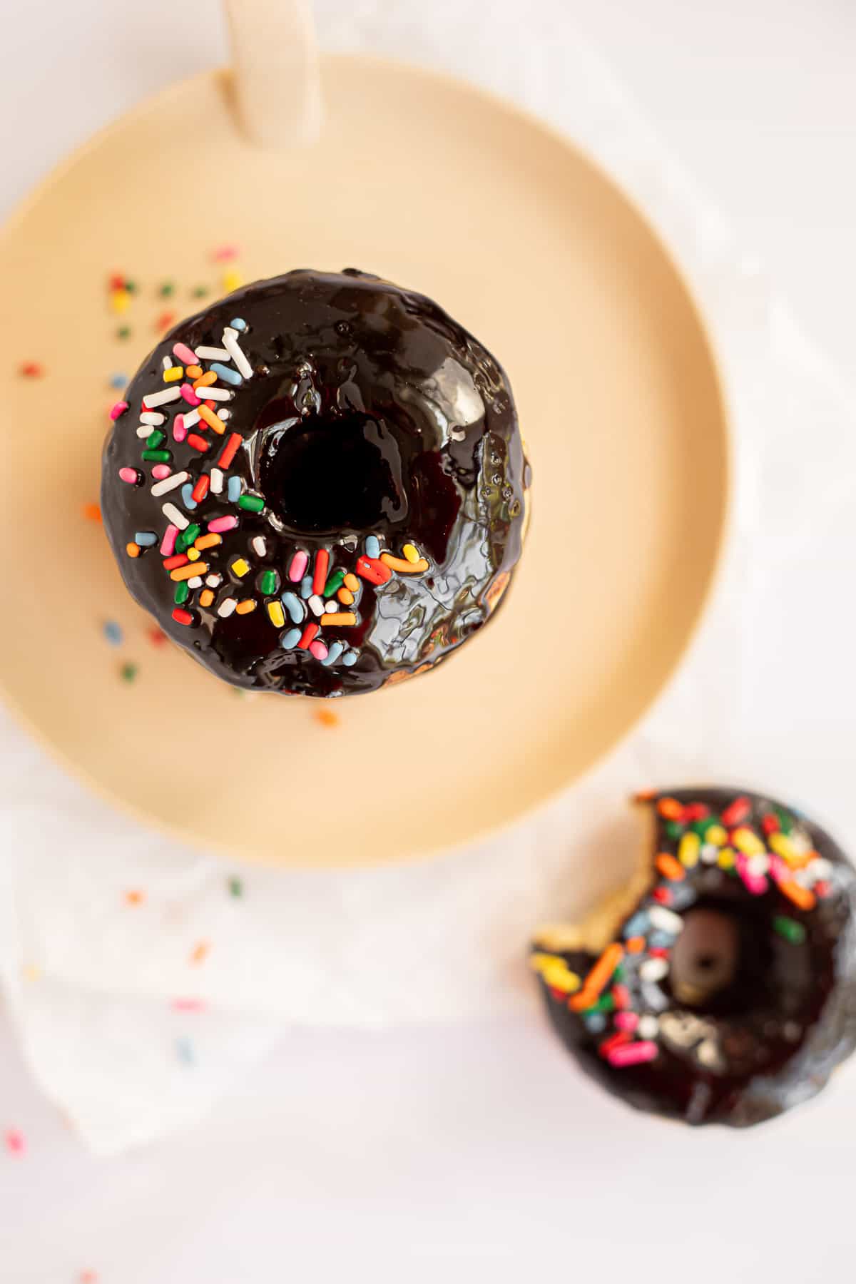 overhead view of two baked banana donuts with a chocolate glaze on a tan plate.