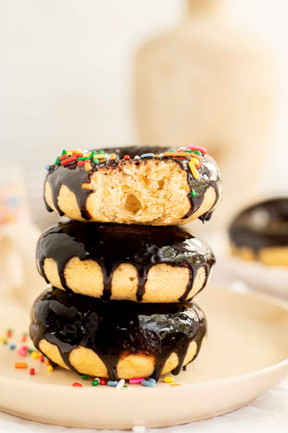 three baked banana donuts with a chocolate glaze stacked on a plate.