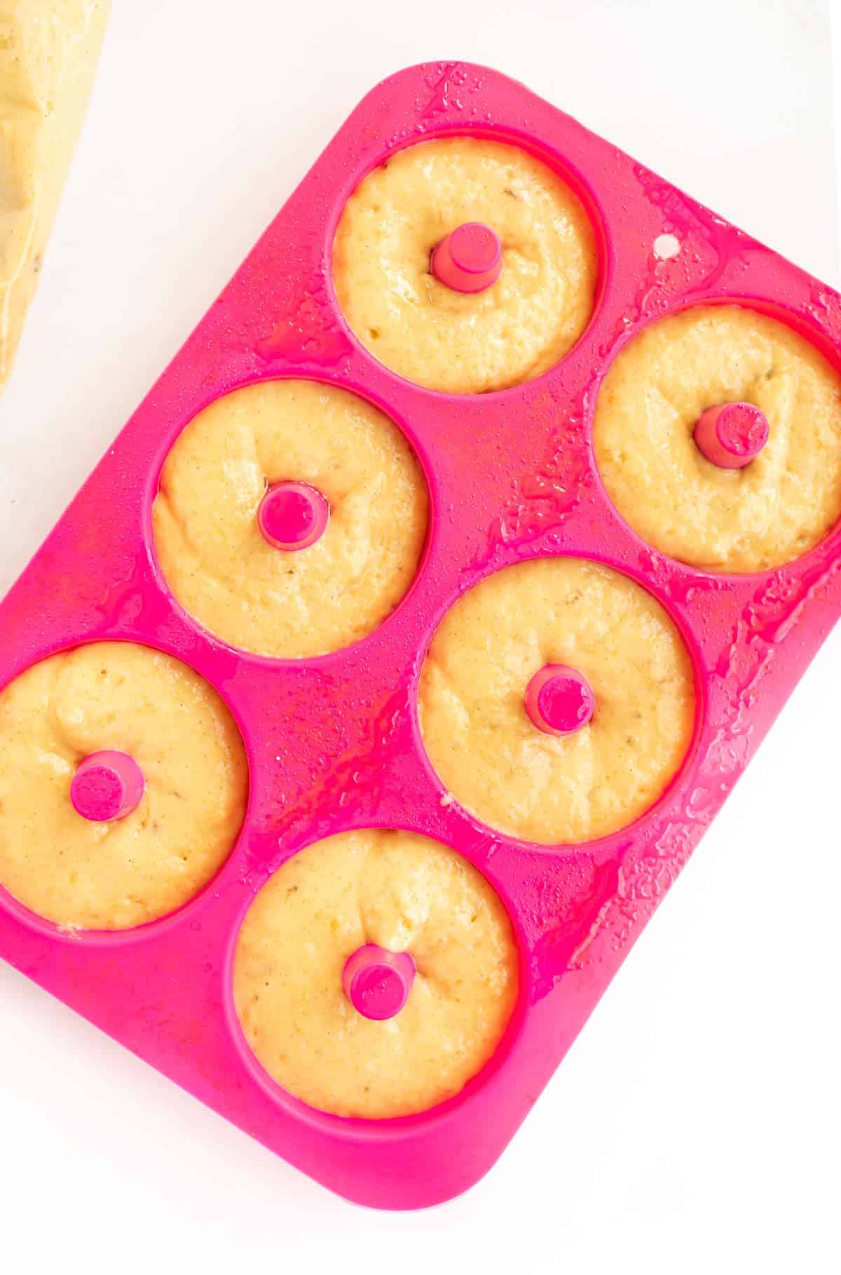 donut batter piped into the wells of a pink silicone donut pan.