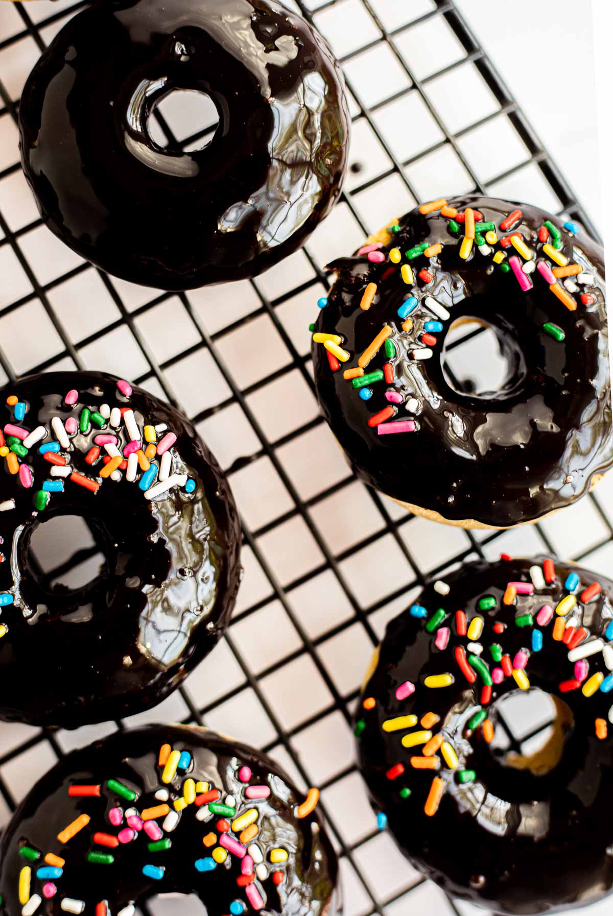 chocolate banana donuts with rainbow sprinkles on a black wire cooling rack.