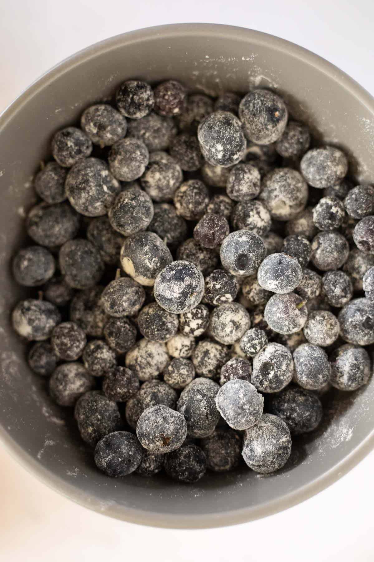 fresh blueberries coated in flour in a gray bowl.