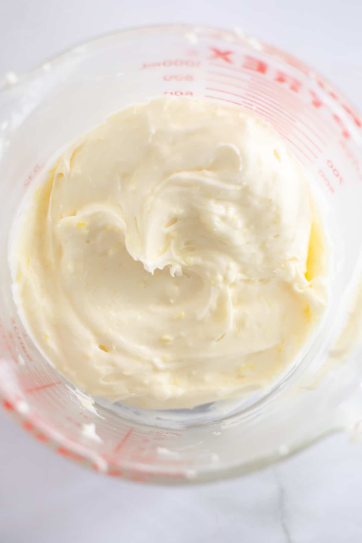 cream cheese frosting with lemon zest in a glass measuring cup.