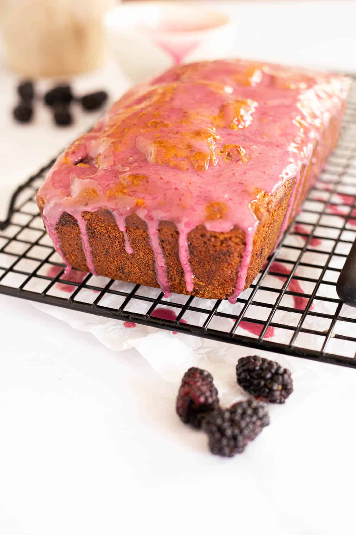 banana bread with a pink blackberry glaze dripping down the sides on a black wire rack.