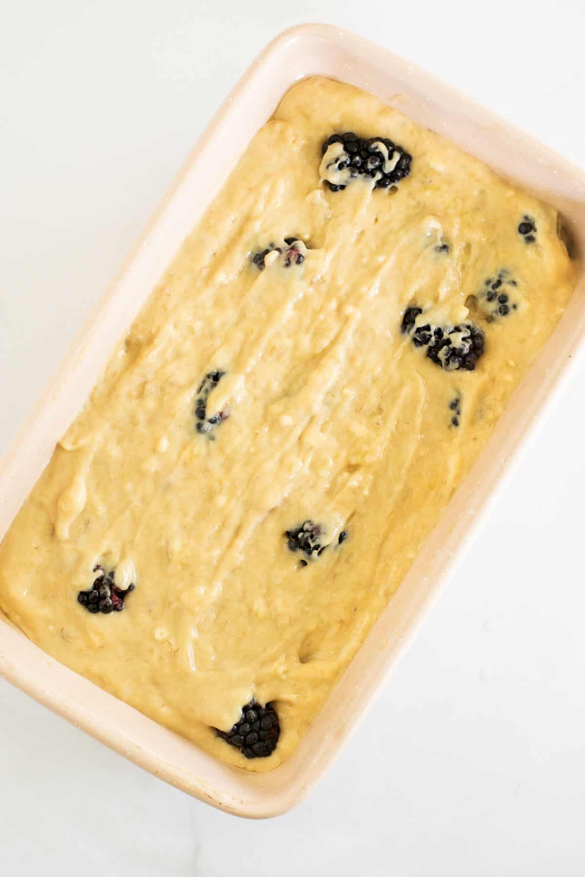banana bread batter with blackberries in a pink loaf pan.