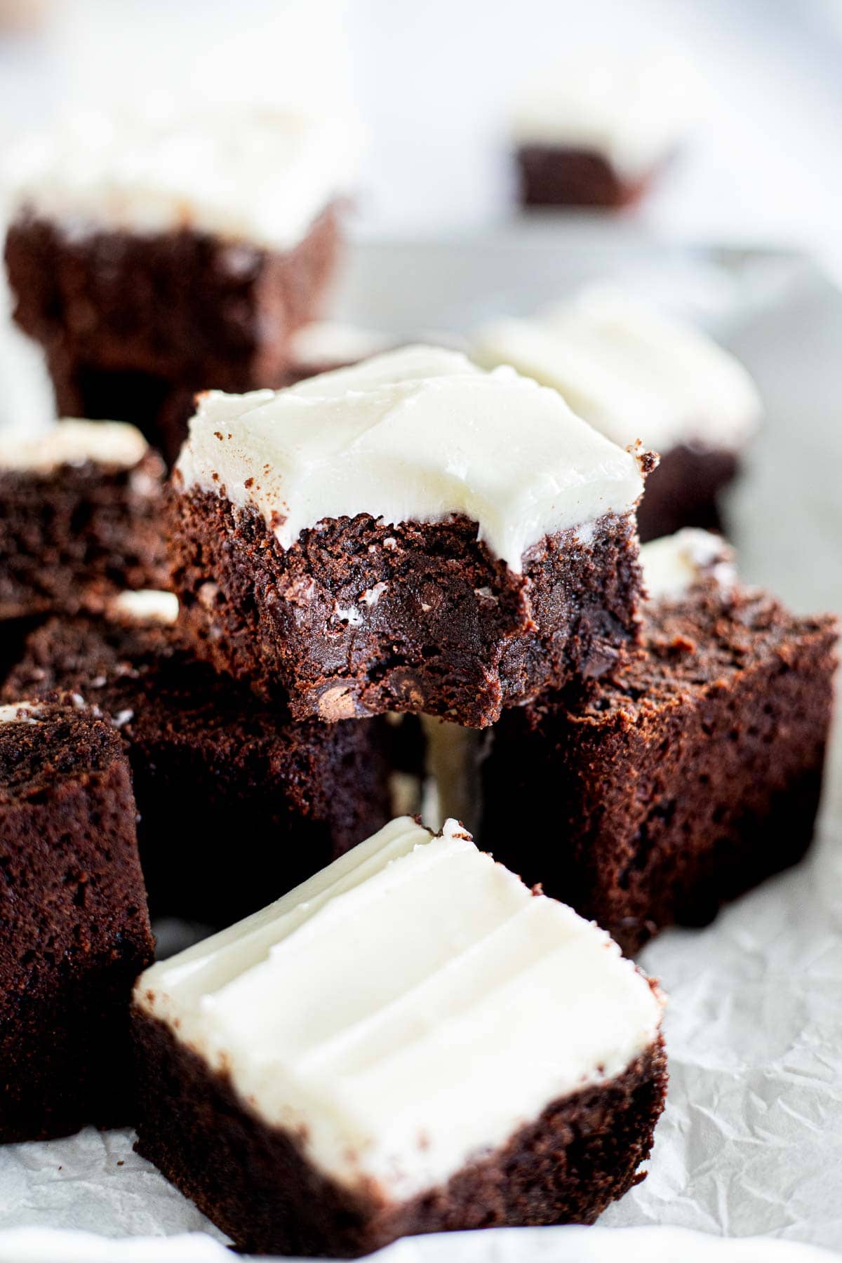 brownie with cream cheese frosting with a bite take out of it on top of other brownies.