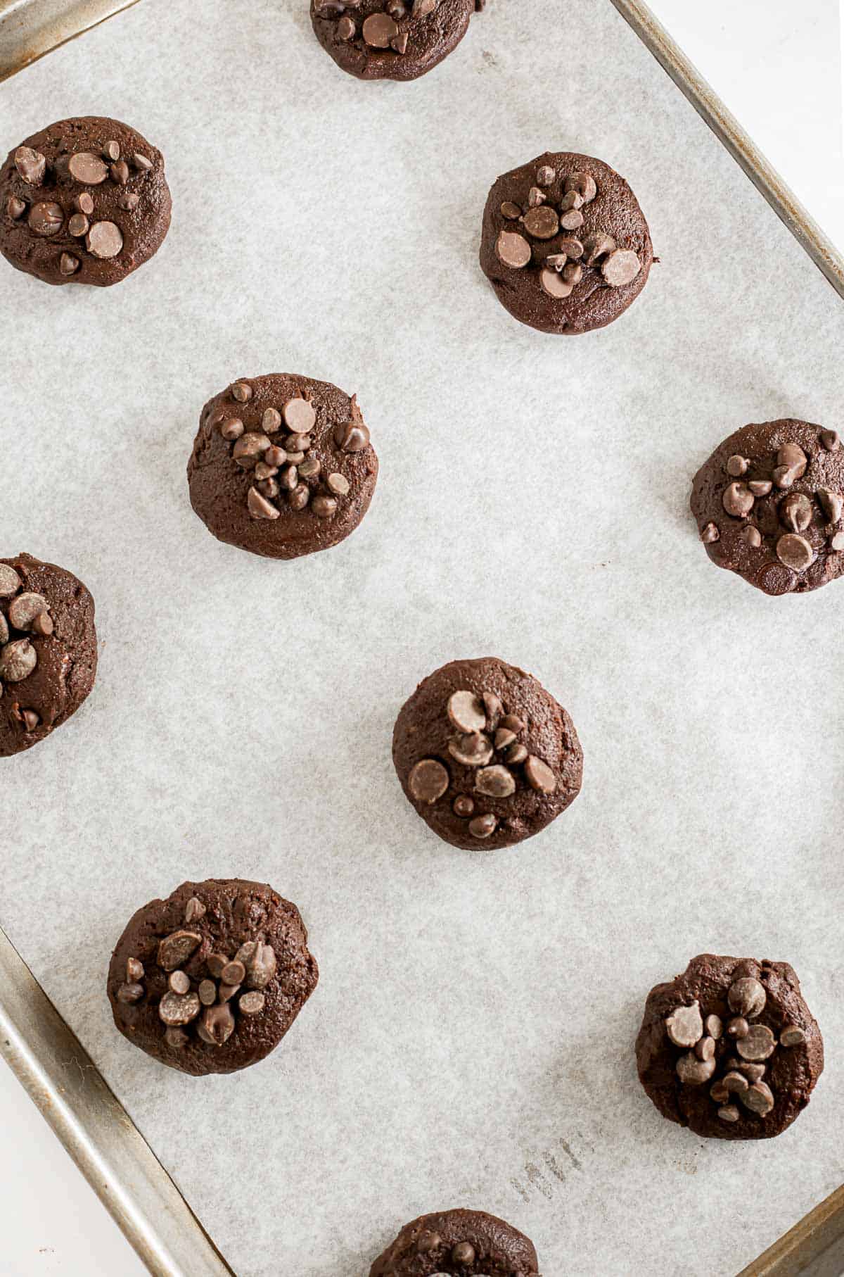 Rolled balls of egg free chocolate cookie dough on a parchment lined baking sheet.