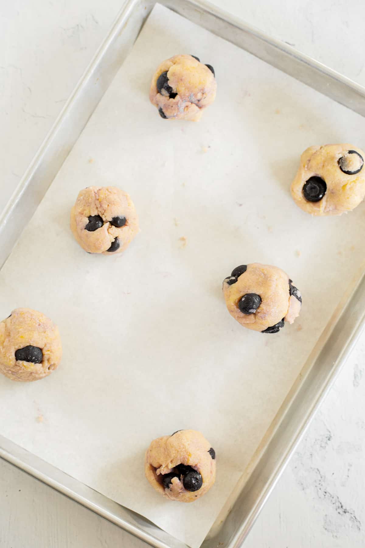 lemon cookie dough with blueberries rolled into balls on a parchment lined baking sheet.