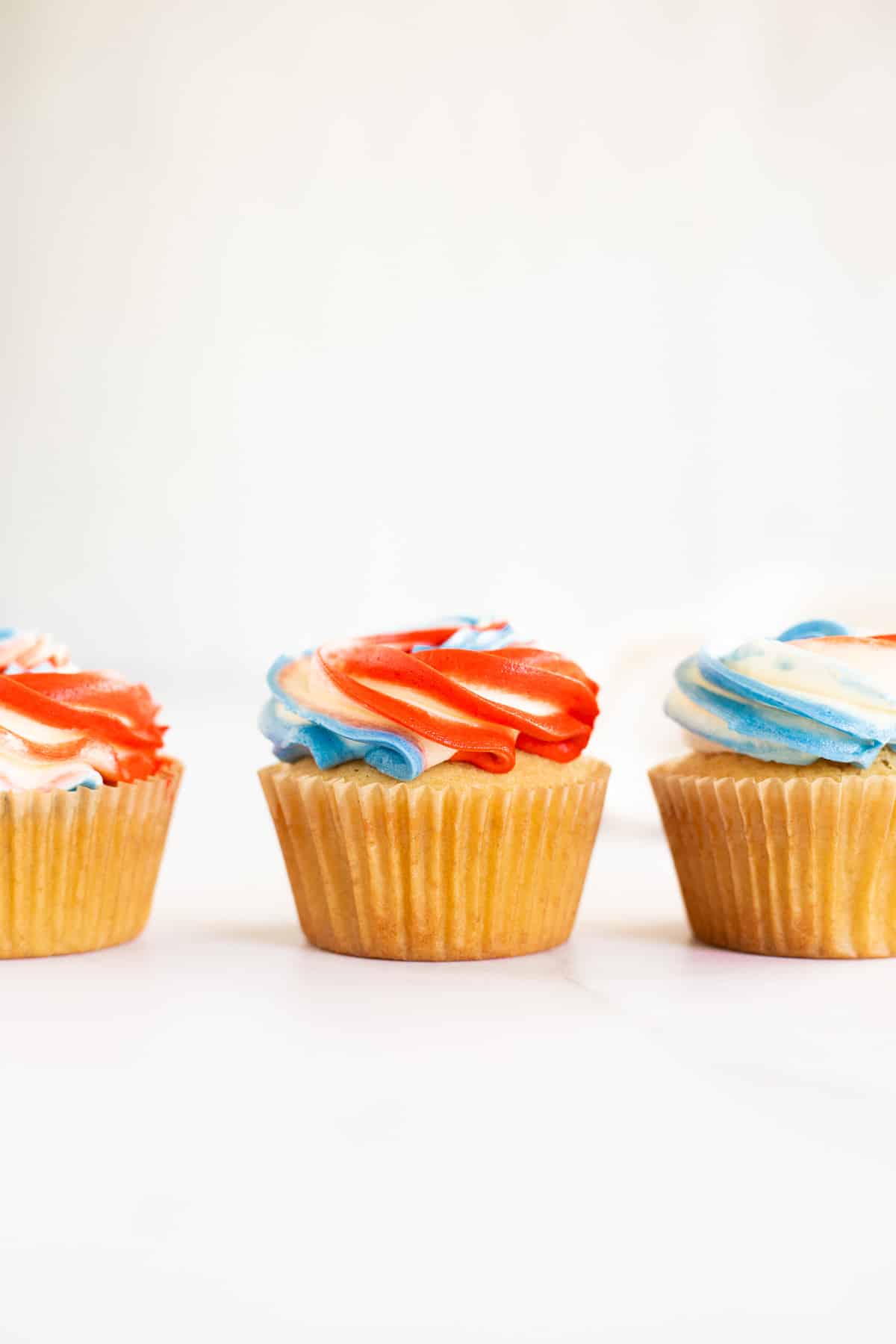 3 patriotic cupcakes on a white backdrop with red, white, and blue frosting.