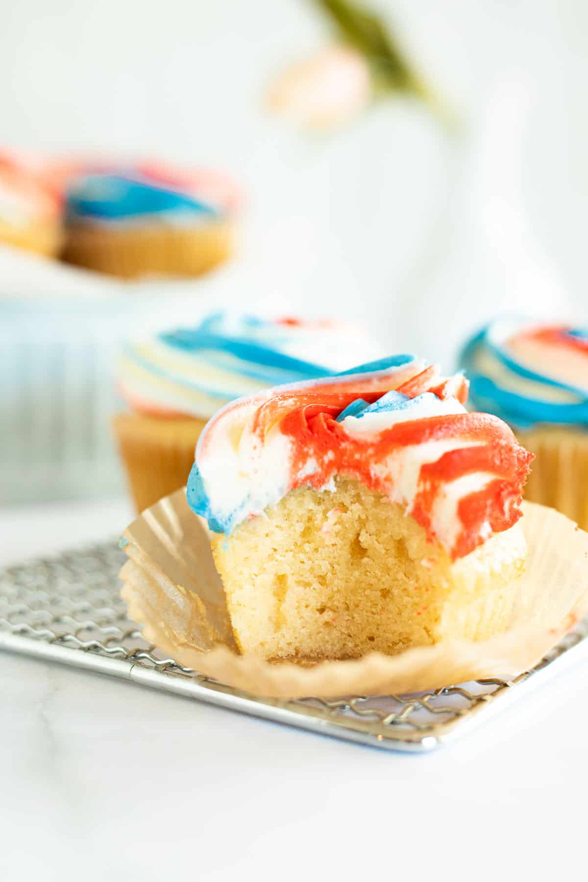 a bite taken out of a vanilla cupcakes with red, white, and blue frosting.