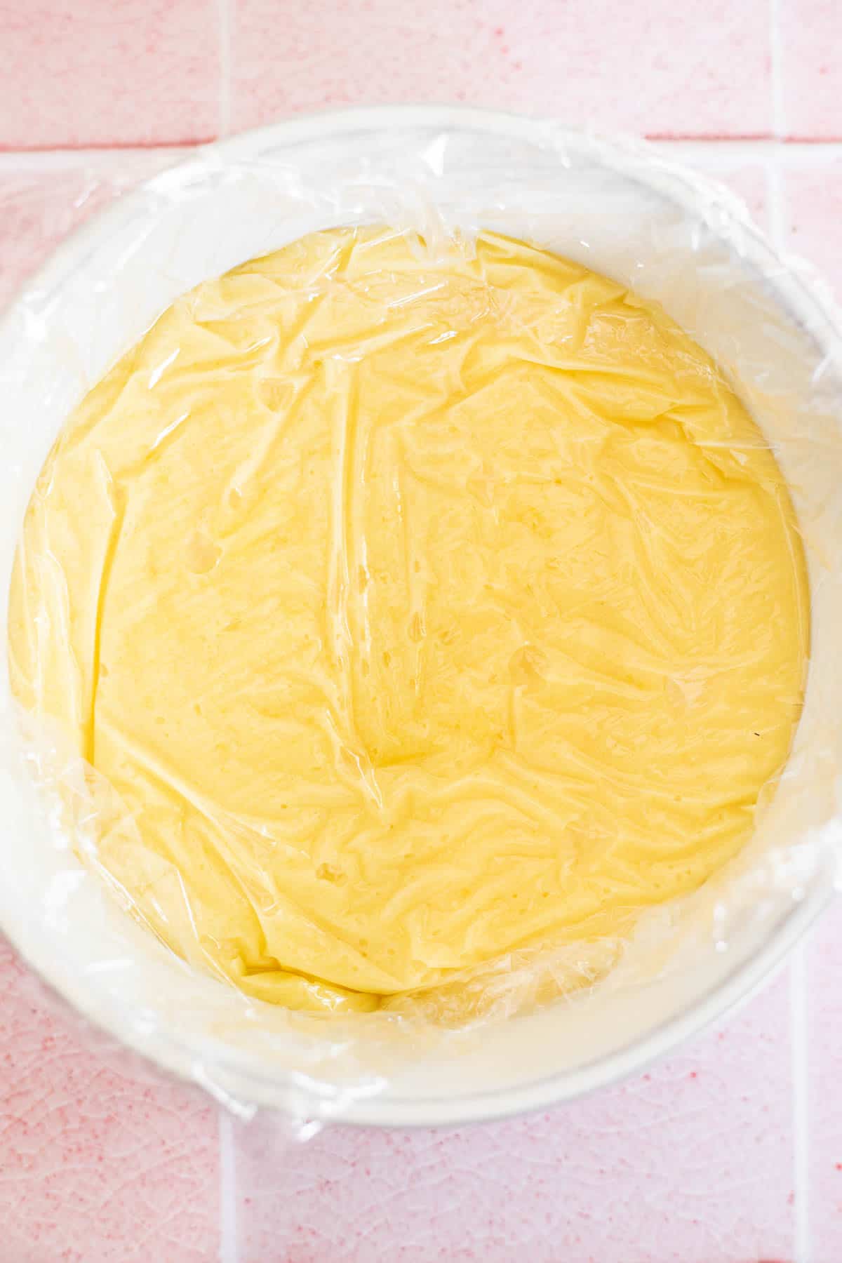a single batch of homemade curd in a white bowl with a layer of plastic wrap over top.