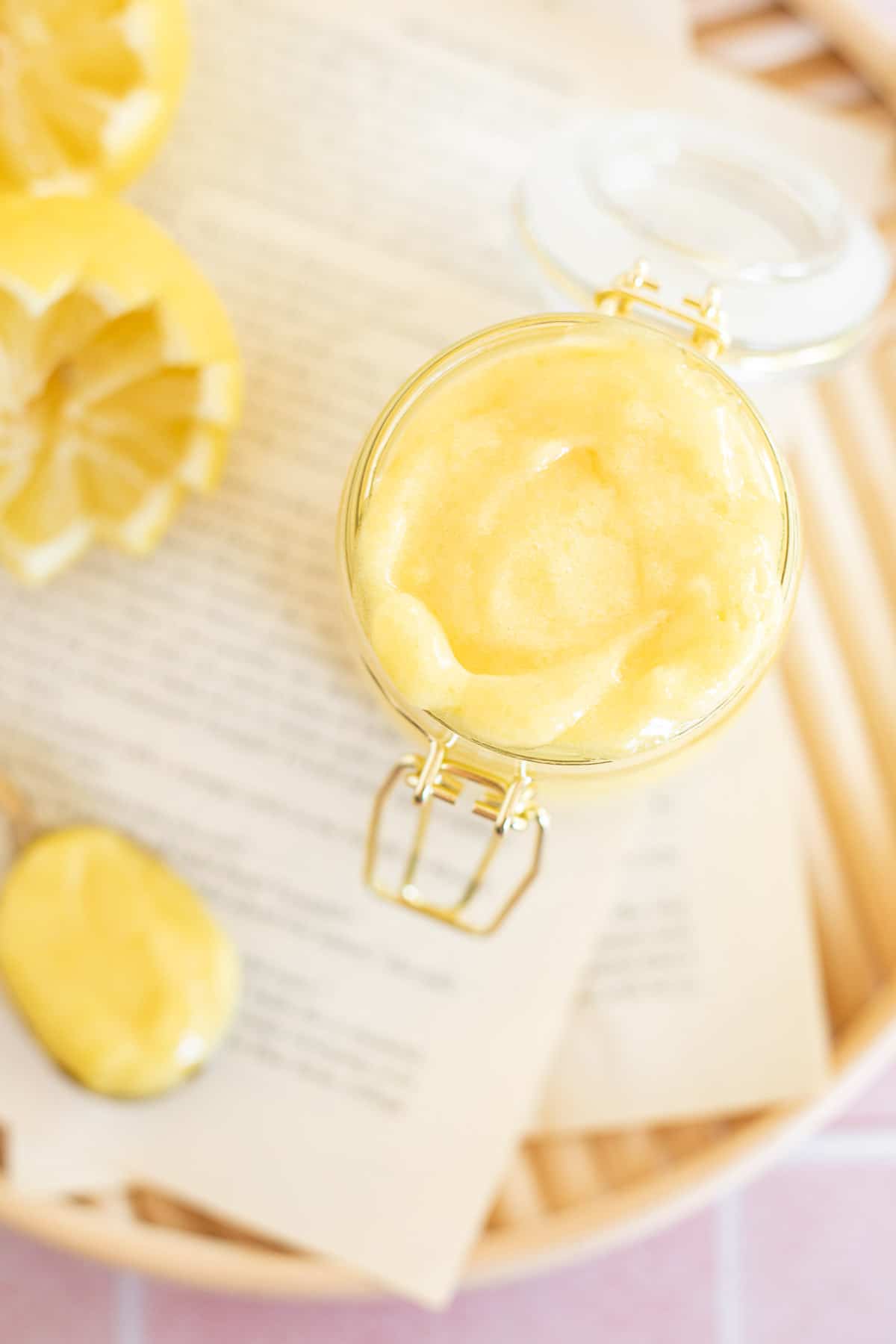 a small glass jar of yellow lemon curd on a wooden serving tray.