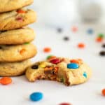 1 M&M cookie with a bite in it next to a stack of cookies on the left.