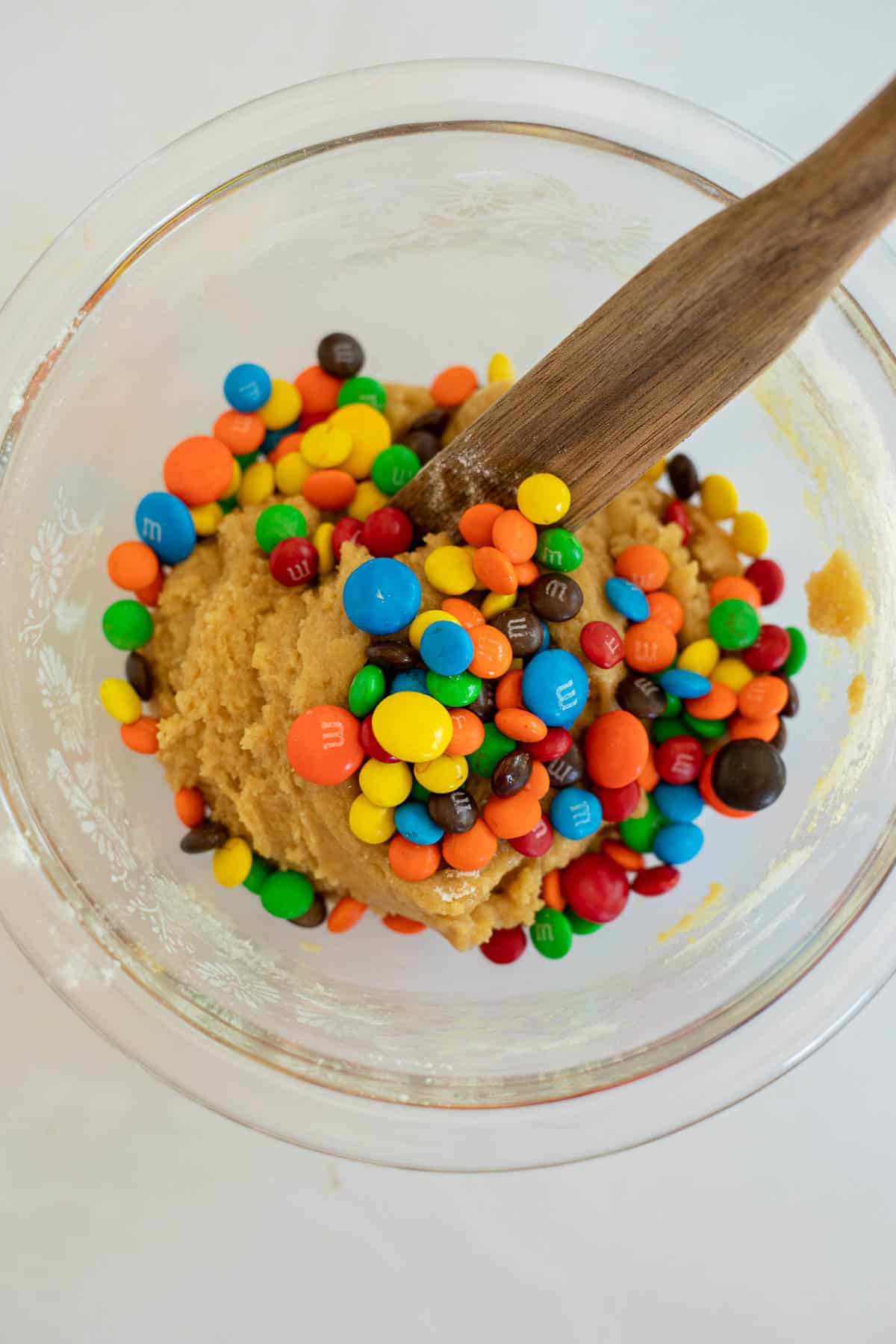 mini and regular M&Ms on top of cookie dough in a glass bowl.