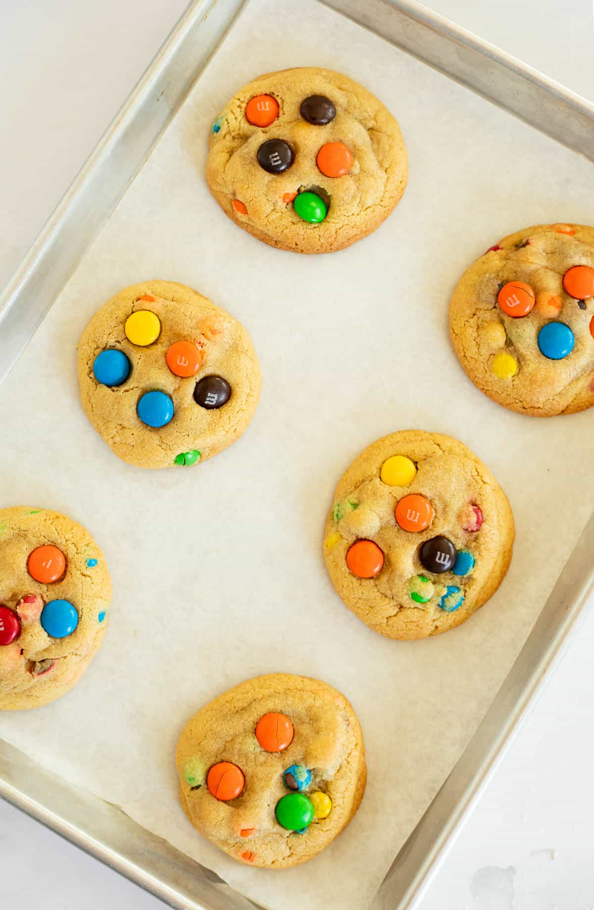 6 M&M cookies baked on a parchment lined baking sheet.