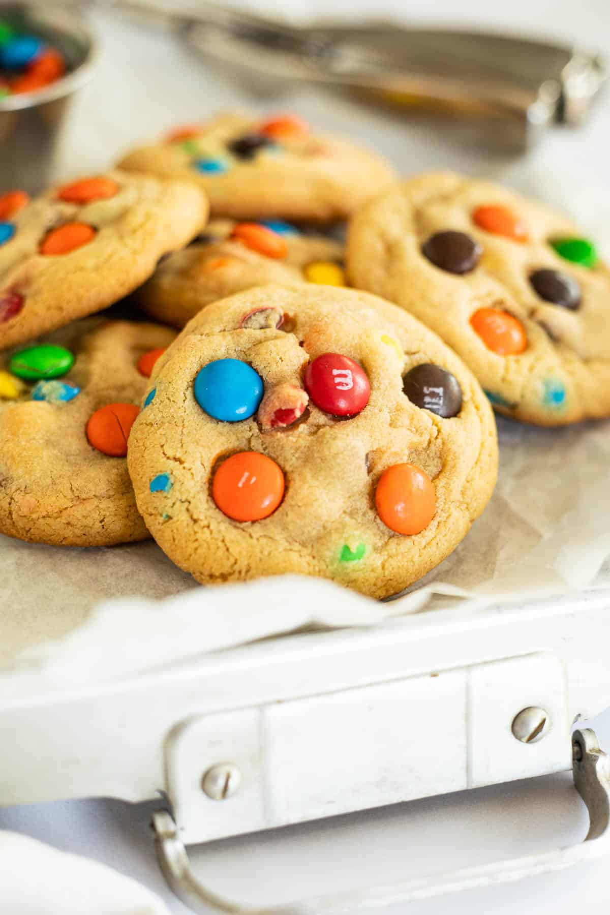 6 M&M cookies in a metal container lined with parchment paper.