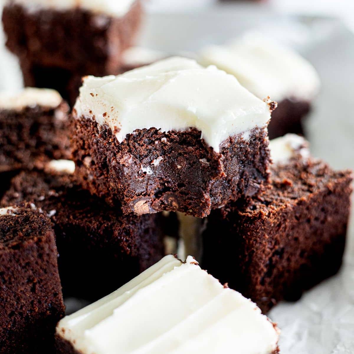 brownie with cream cheese frosting with a bite take out of it on top of other brownies.