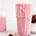 Cherry milkshake in a glass with whipped cream and a fresh cherry.