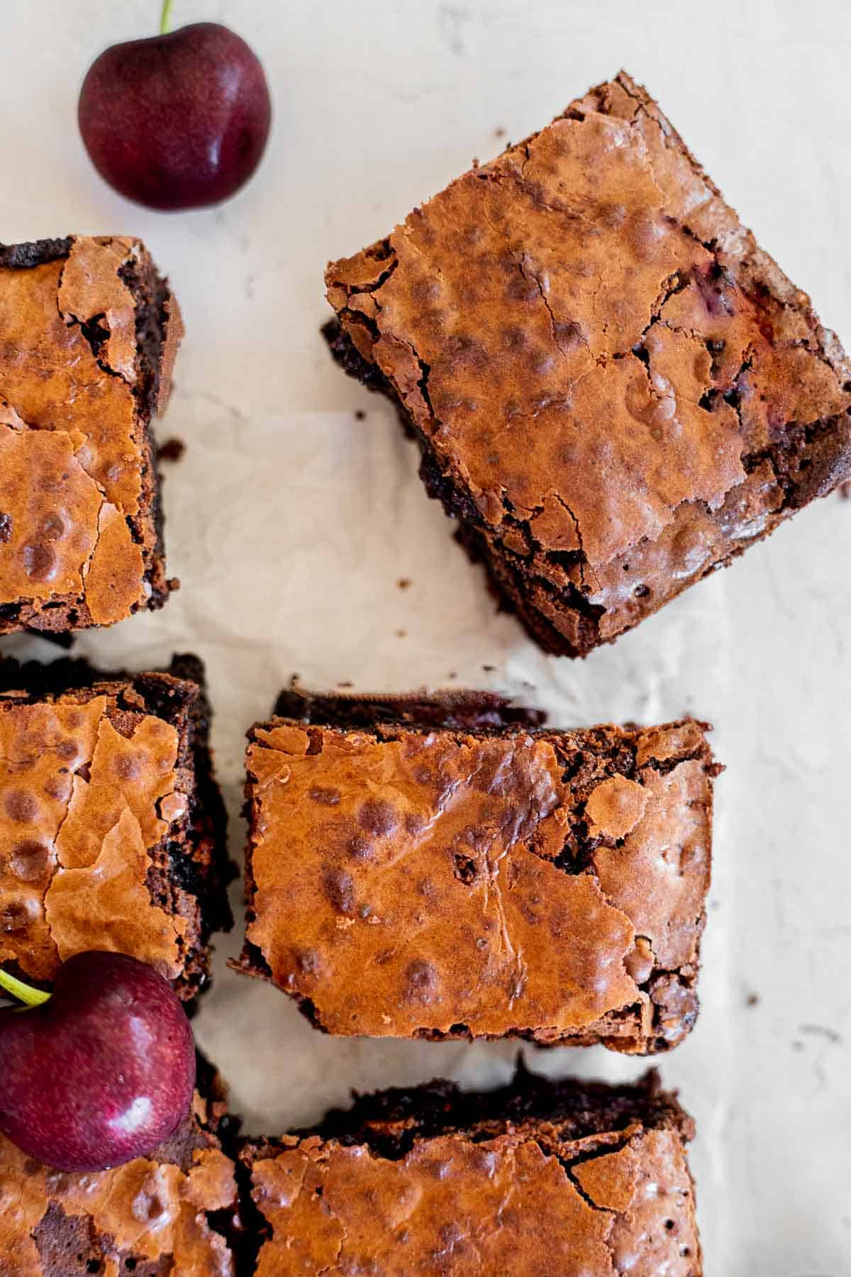 brownies with cherries cut into squares on parchment paper.