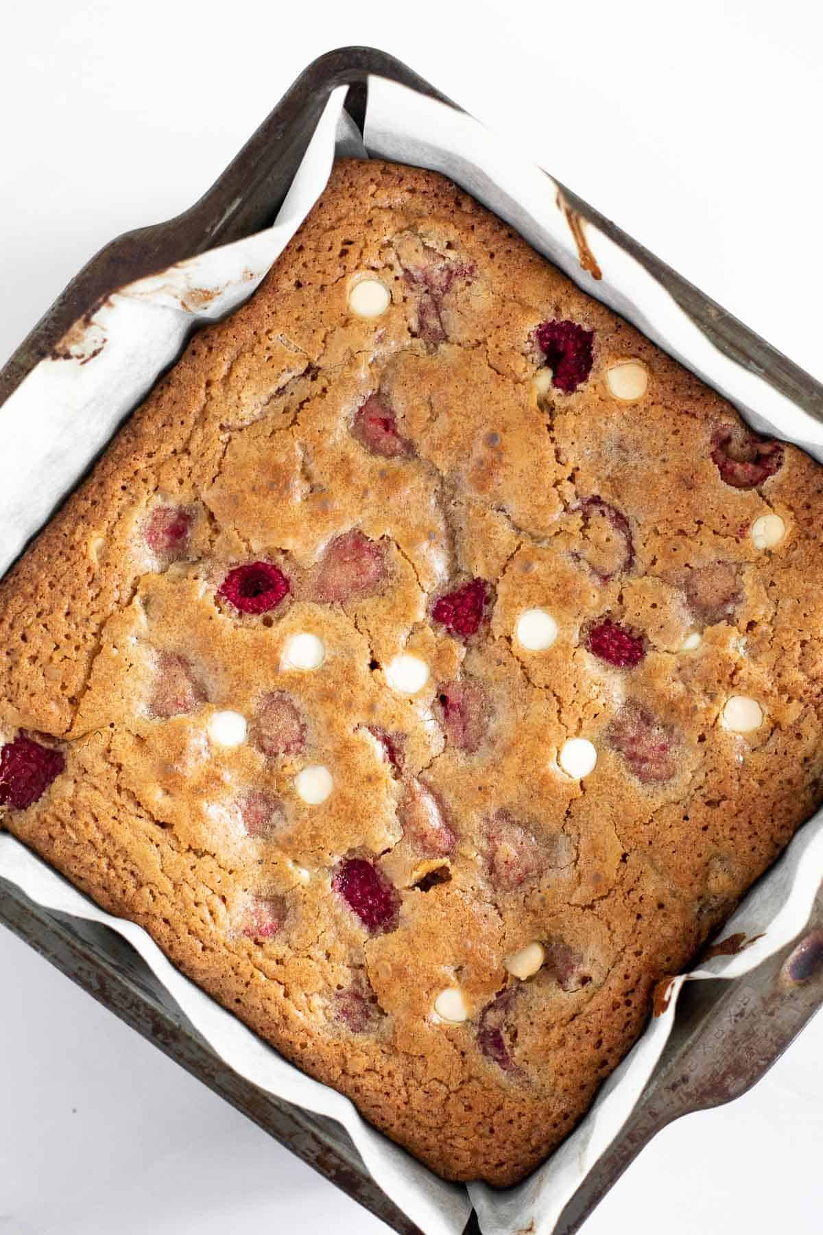 Baked blondies with white chocolate chips and raspberries in a metal baking pan.
