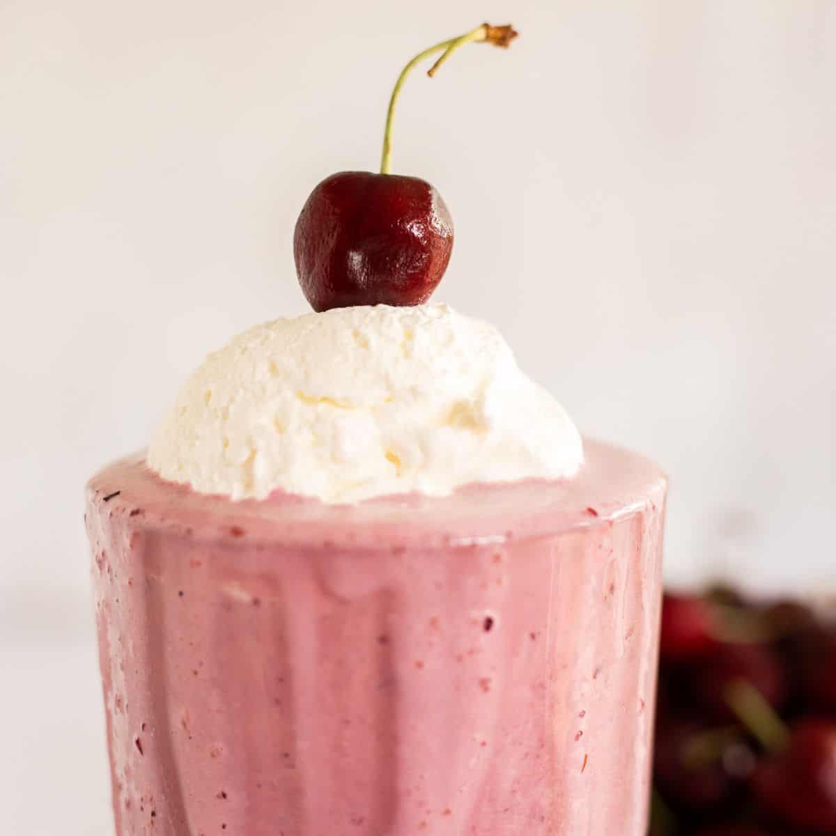 cherry milkshake in a glass topped with whipped cream and a fresh cherry.