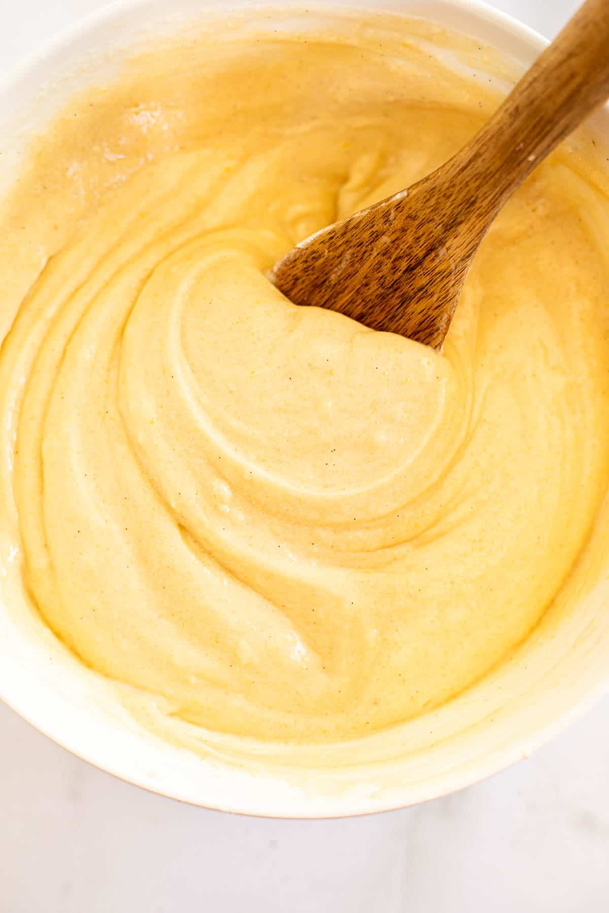 smooth vanilla cupcake batter in a white mixing bowl with a wooden spoon.