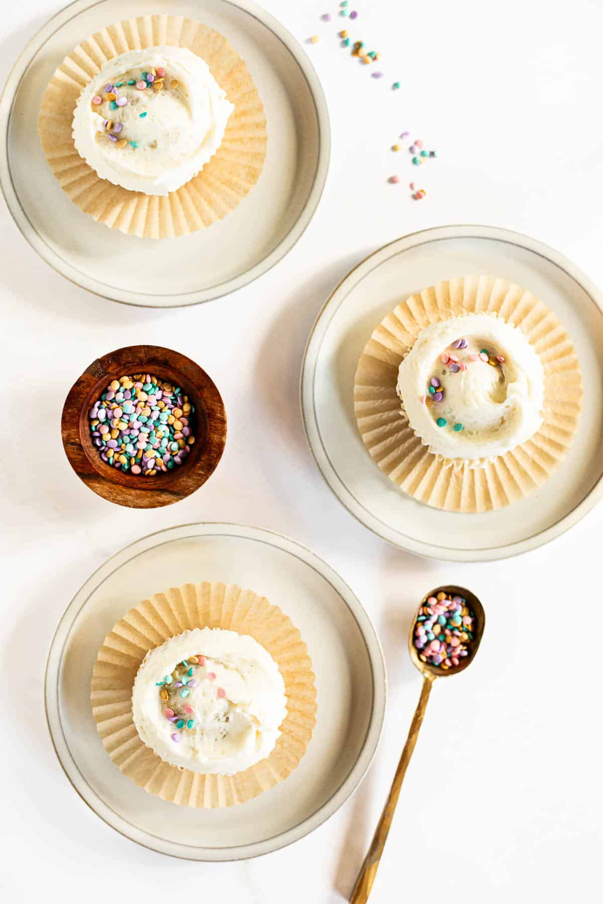3 moist vanilla bean cupcakes on 3 white plates topped with sprinkles.