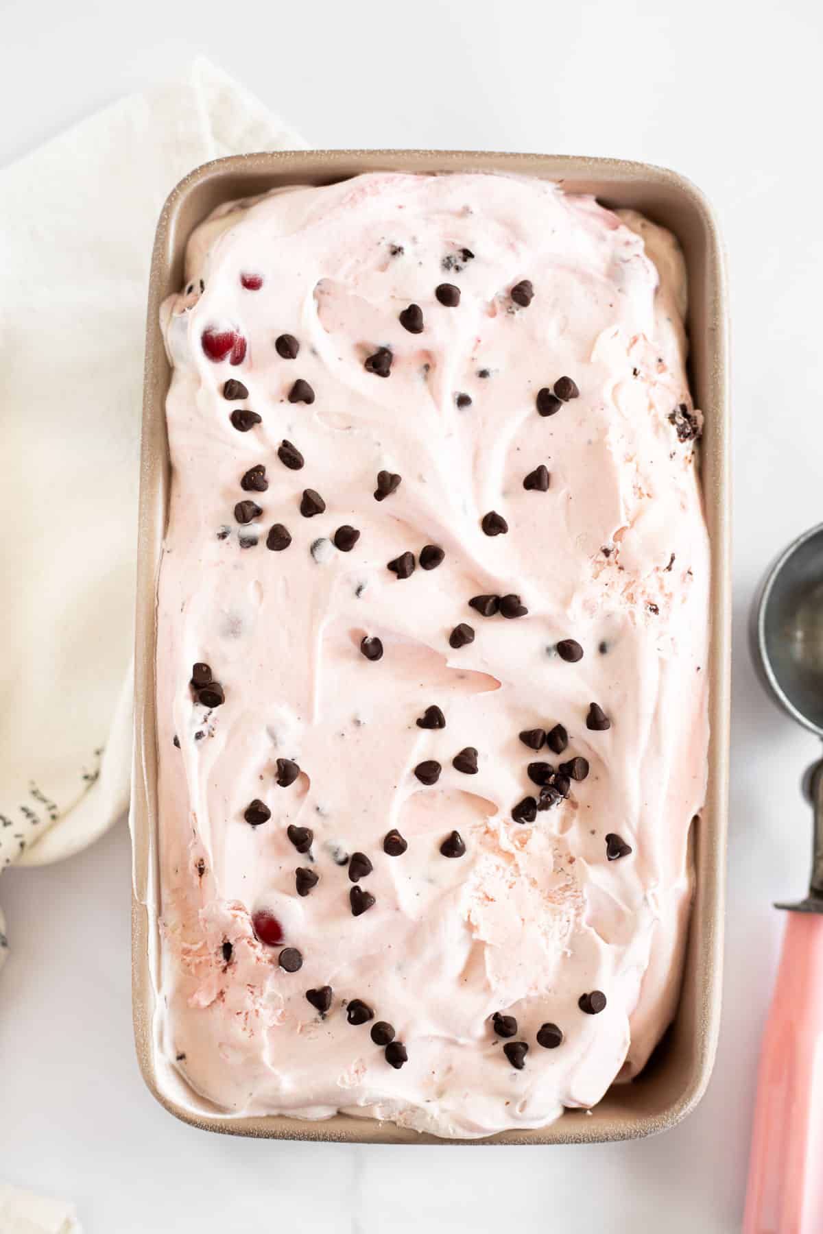 no churn black forest ice cream topped with mini chocolate chips in a loaf pan.